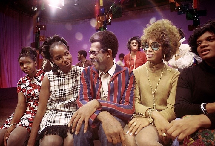 A colorfully clad Ellis Haizlip is flanked by four female guests on the set of Mr. SOUL!