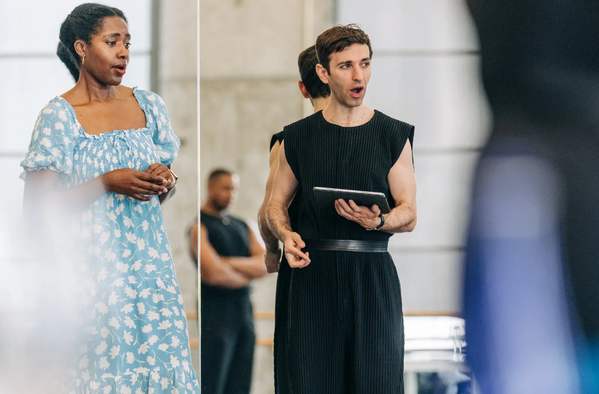 Man and woman mid note singing in rehearsal clothes.