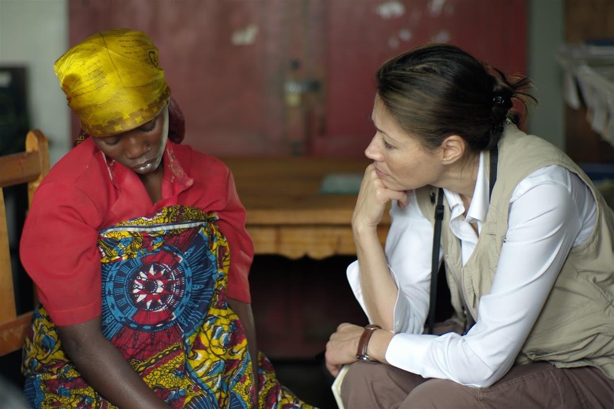 Ann Curry hand on chin with woman in brightly colored headwrap and dress.