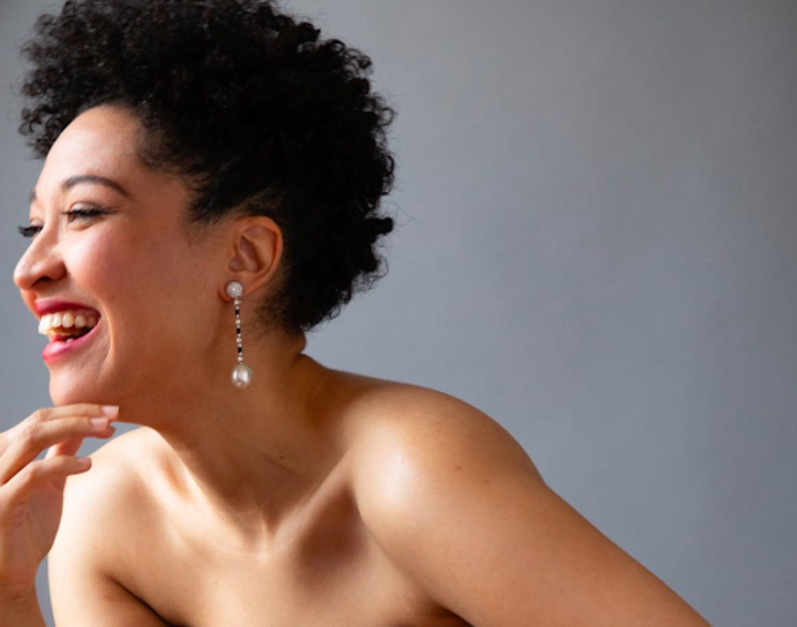 Artsist smiles, looks away from camera, grey backdrop.