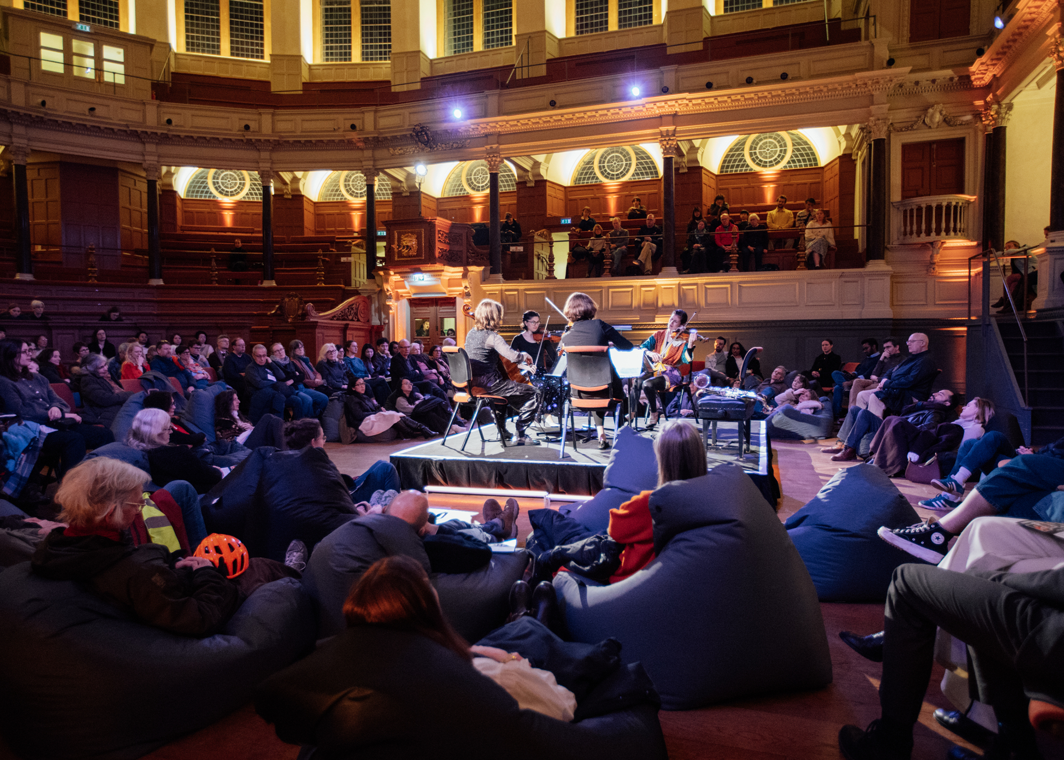 Performers on a small stage surrounded by an audience. People sit on the floor.