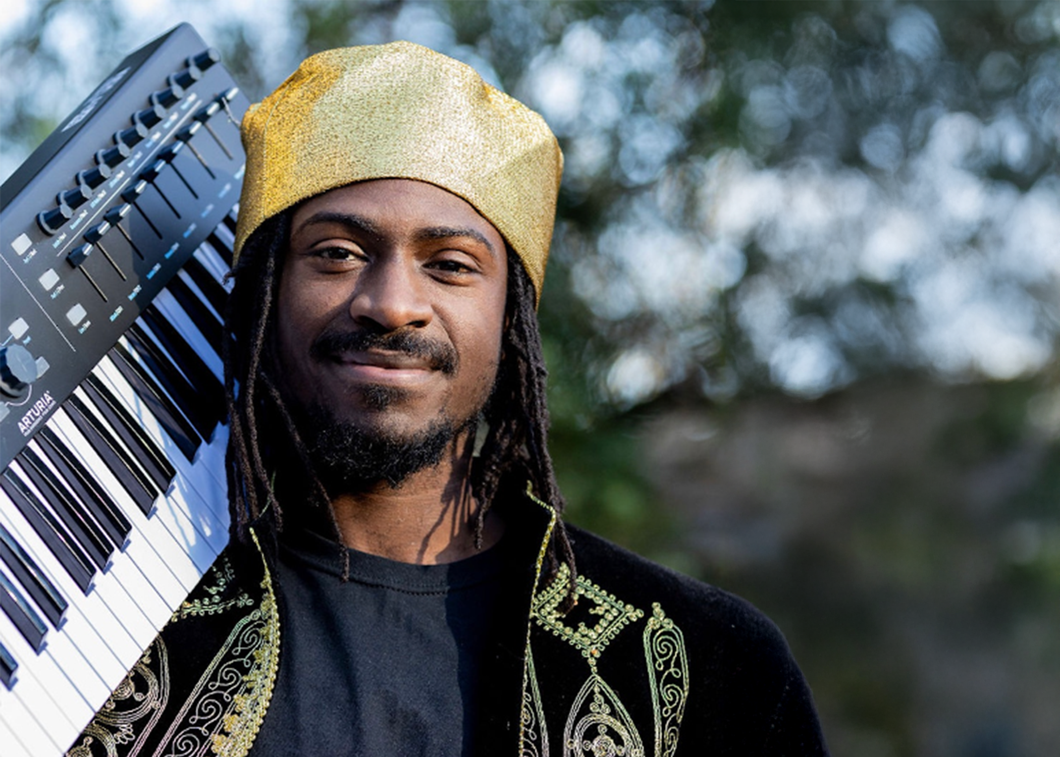 Artist holding a keyboard and wearing a hat.