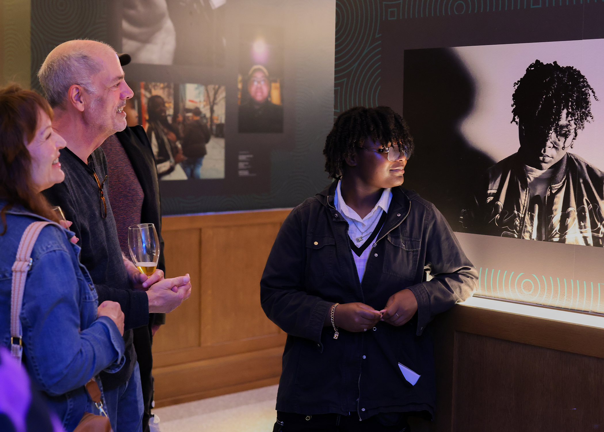 Two people admire student artwork. The artist is next to their photograph.