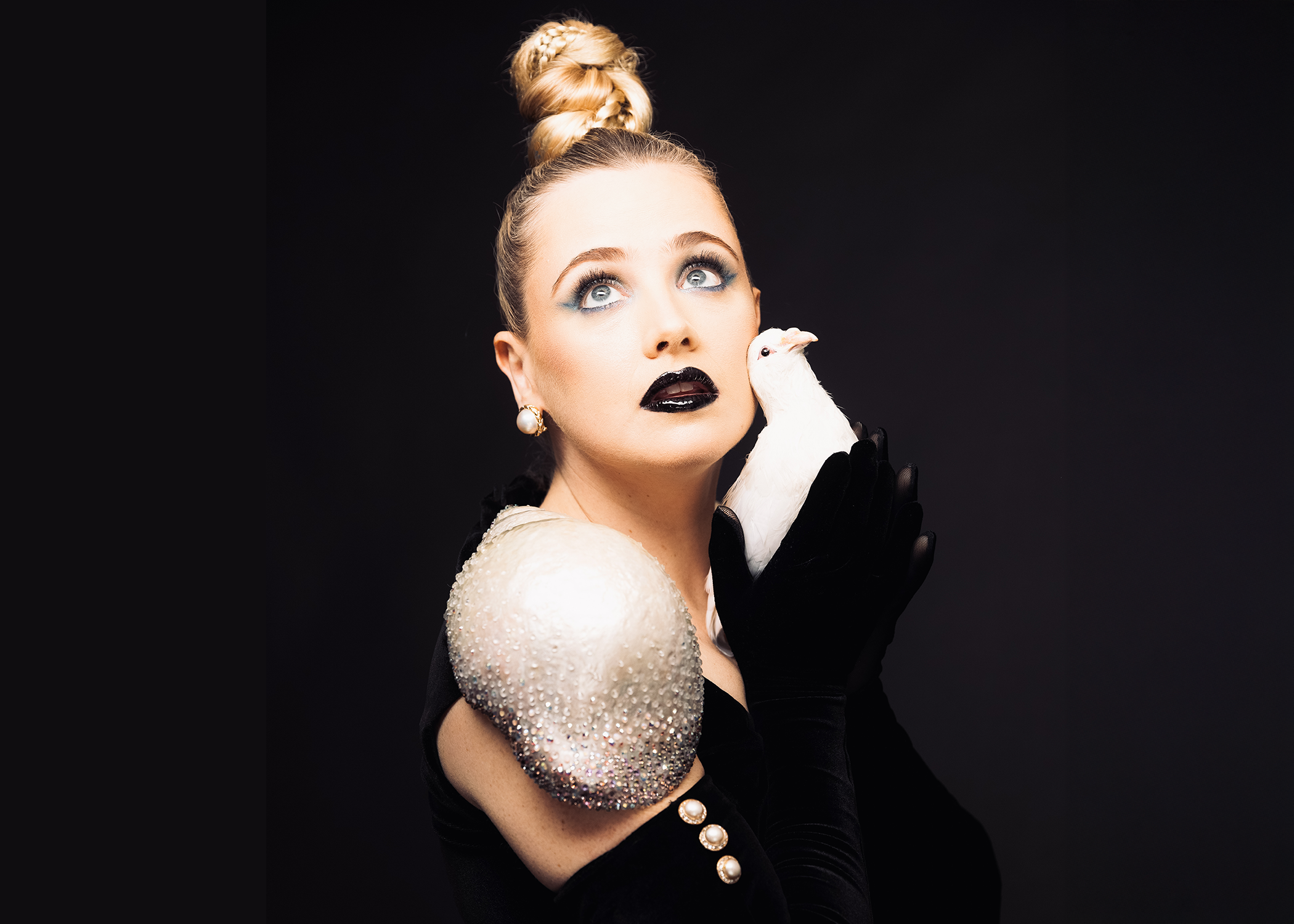 Liz Toonkel wears black with an off the shoulder gown. She holds a white bird.