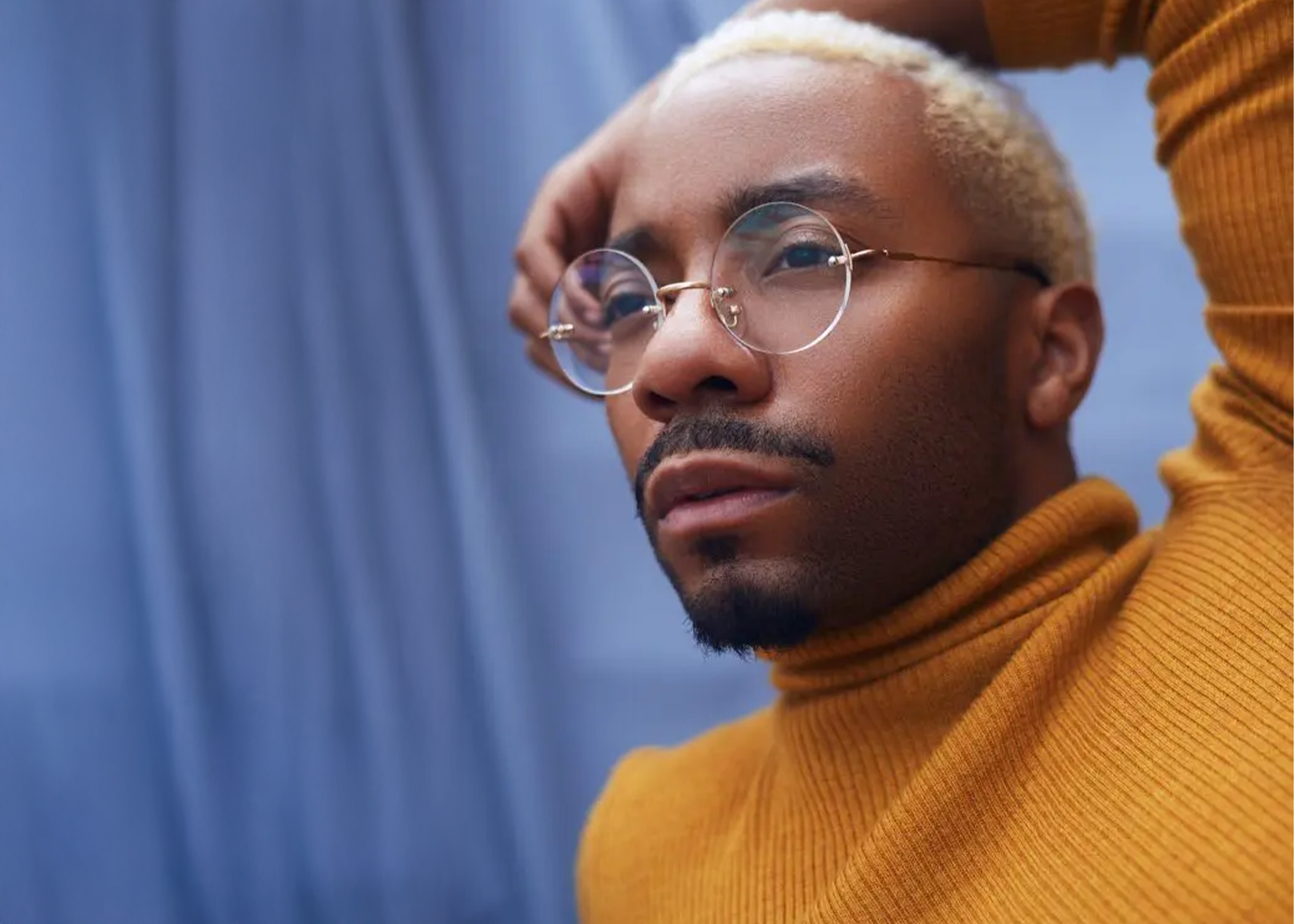Roderick George: Headshot, wearing orange sweater with arm draped over head.