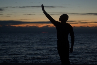 Silhouette of a man on a beach against a dusky horizon reaching heavenward