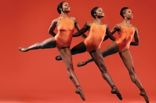 Three women in mid jump, defined muscles, wearing orange on an orange backdrop.