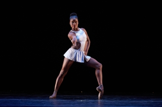 Dance Theatre of Harlem female dancer in a white costume striking a post on a dark stage