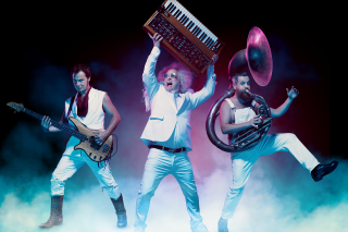 Three band members in high energy dance with smoky vapor wave scene.