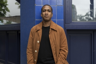 In rust color jacket in front of blue tile.