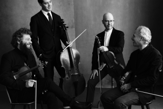Four musicians in dialogue with each other. Black and white. One stands.