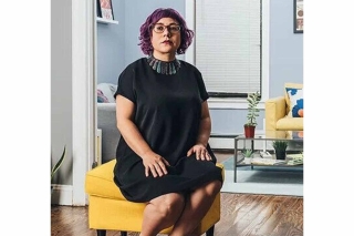 Portrait of a woman with glasses and purple hair, sitting on a yellow chair