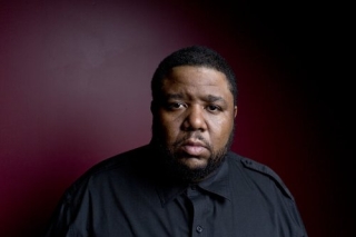 Portrait photo of a man in a black button down with a maroon background