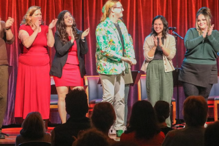 People stand on stage in front of a red curtain. Applause.
