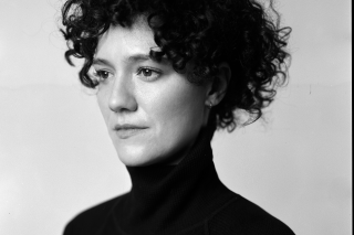 Black and white headshot. Curly hair and black turtleneck.