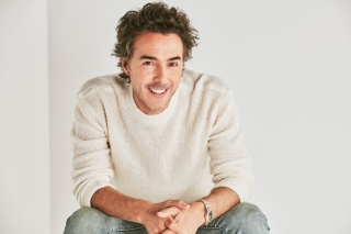 Shawn Levy wearingf white shirt and jeans, seated, smiling.
