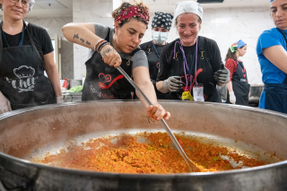 People gather around a large bowl of food. Chef stirs the orange food.