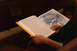 'The Gift' book lays open to an illustrated page on the lap of someone reading it