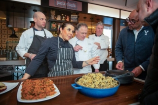 Chef with plates of food instructing other chefs. 