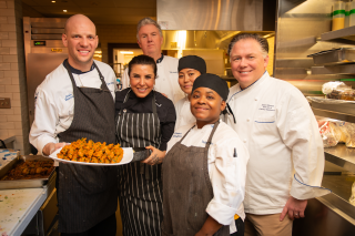 Hospitality chefs and Global Fellow in the kitchen holding a dish.