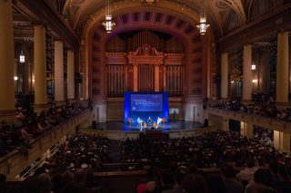 Long view of Woolsey Hall stage with a packed audience. 