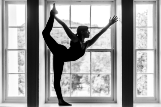 Person balancing on one leg, silhouette in front of a window.