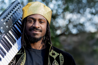 Artist holding a keyboard and wearing a hat.