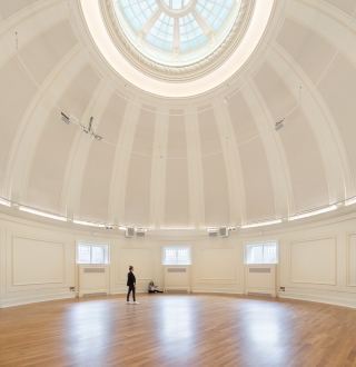 A person stands in the brightly lit interior of the dome, its floors a polished wood.