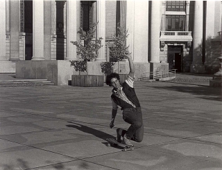A black and white photo of Dan Gesmer skateboarding through the plaza.