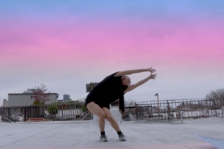 Dancer extends her arms on a rooftop at dusk