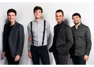 Four members of Sandbox Percussion standing, smiling at the camera