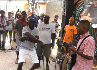 A person dancing on a bustling street, accompanied by drummers