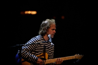 Bryce Dessner sitting in a chair performing guitar on stage