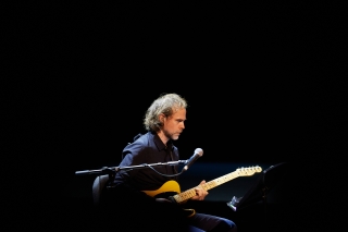 Bryce Dessner sitting in a chair performing guitar on stage