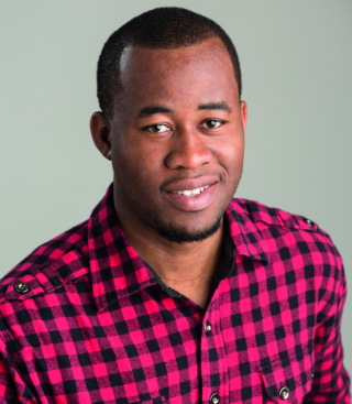 Obioma smiling in a headshot, wearing a pinkish red and black plaid shirt.