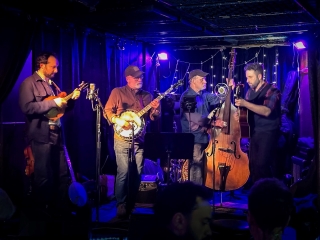 Band of four people with dark background and purple lighting.