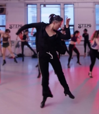 Mid dance move, wearing black, in a dance classroom.