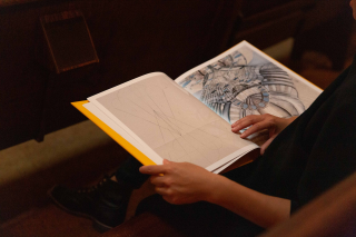 'The Gift' book lays open to an illustrated page on the lap of someone reading it