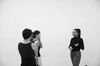 Sidra Bell in conversation with two other dancers. Black and white image in a white studio.