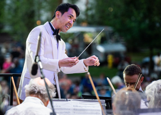 Conductor in white clothing, surrounded by musicians.